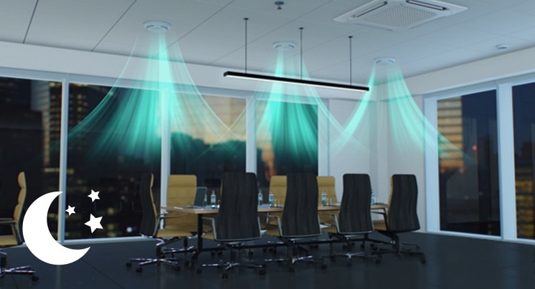 Three circular ceiling-mounted ducts dispense a visible blue airflow into a conference room on a dark night.