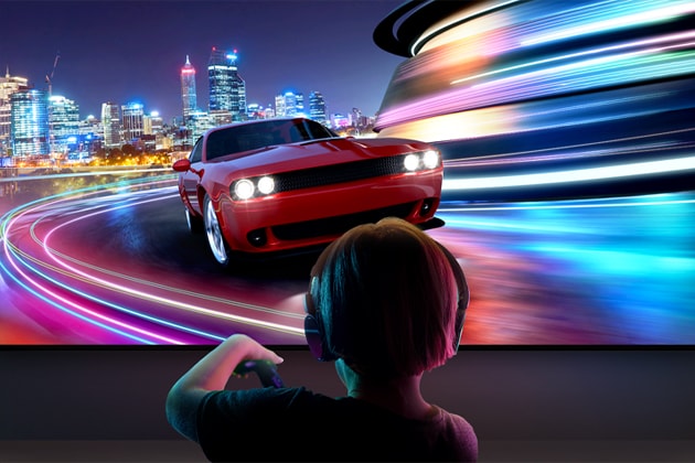 A young boy wearing headphones is seen from behind playing a car racing game on a large LG TV. 