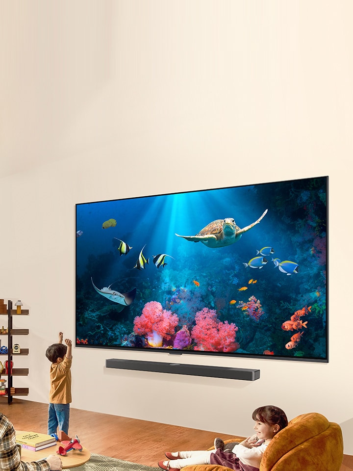 An image of a family watching a bright aquatic scene on an LG QNED TV and an LG Soundbar in a bright and natural living space.