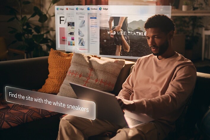 Ein Mann sitzt auf einer Couch und benutzt einen Laptop. Auf einer virtuellen Benutzeroberfläche wird der Text „Finde die Seite mit den weißen Turnschuhen“ angezeigt und über dem Laptop-Bildschirm schweben mehrere Browser-Registerkarten.