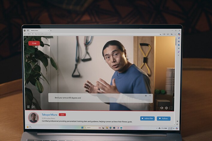 Auf dem Laptop-Bildschirm wird eine Live-Übertragung angezeigt, die einen sprechenden Mann zeigt. Während er spricht, erscheinen am unteren Bildschirmrand Untertitel mit automatischen Übersetzungen.