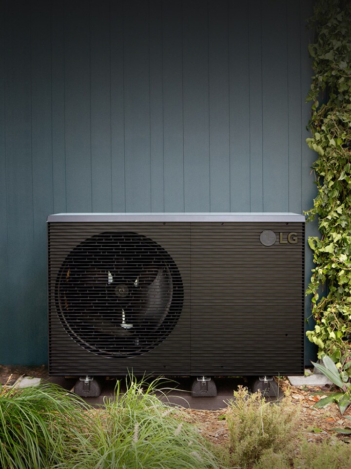 Bomba de calor ar-água LG THERMA V R290 Monobloco, unidade externa de cor preta é colocada na parede verde externa da casa.	