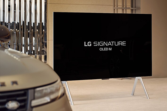 LG SIGNATURE OLED M4 num stand na Range Rover House, junto ao Range Rover Sport SV, e um botão de reprodução na parte inferior da imagem.