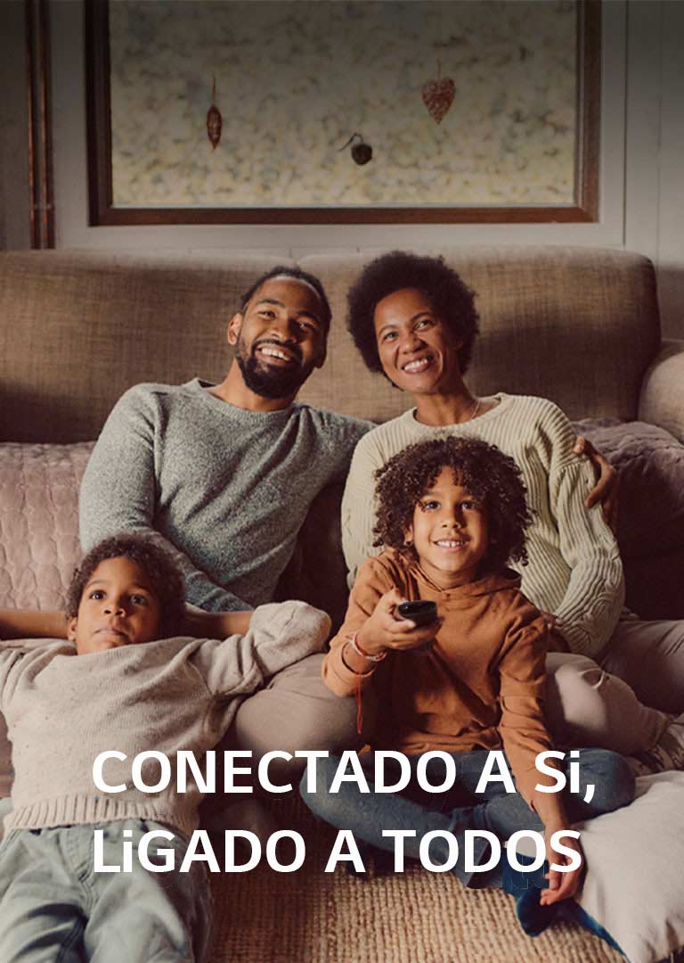 Uma imagem de uma família de quatro pessoas sentadas no chão em frente a um sofá castanho acolhedor, olhando em frente e rindo enquanto vêem televisão. As palavras “Syncs to you, open to all” (Sincroniza-se consigo, aberto a todos) sobrepõem-se à imagem num tipo de letra branco. 