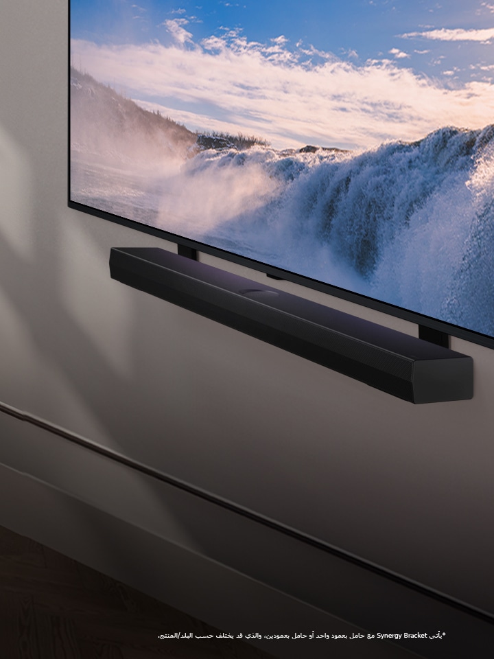 يُوضع تلفزيون LG TV ومكبر الصوت Soundbar في منظور مائل مثبت على الحائط. على التلفزيون، تٌعرض لقطة مقرّبة لشلال شاسع وضوء الشمس الناعم يتدفق على الحائط والتلفزيون ومكبر الصوت soundbar. وينص إخلاء المسؤولية على ما يلي: "يأتي Synergy Bracket مع حامل بعمود واحد أو حامل بعمودين، والذي قد يختلف حسب البلد/المنتج."