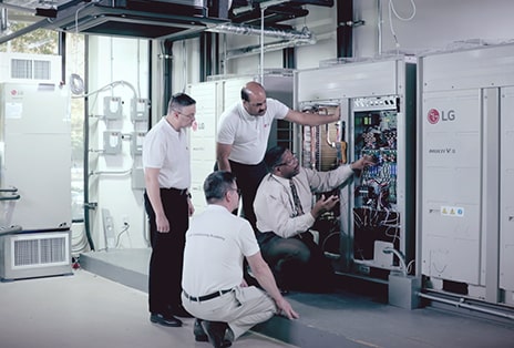 Four experts are inspecting one of the LG MULTI V i machines installed next to the wall, carefully checking its performance and key components.