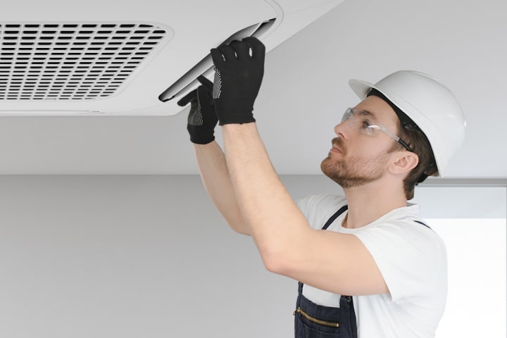 A technician is installing or servicing the LG ceiling-mounted cassette air conditioning unit, wearing a safety wear.