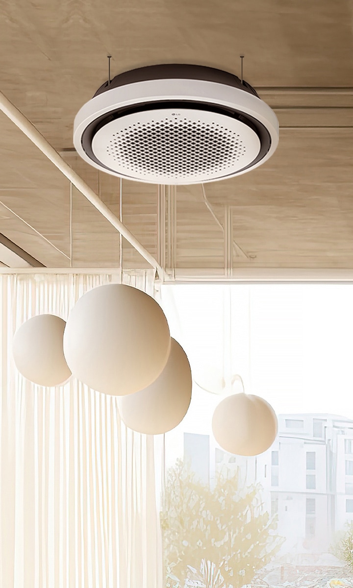 The LG Round Cassette is centrally installed in a sunlit room with high ceilings, blending modern design with the room's elegant wood accents and large hanging light fixtures. 