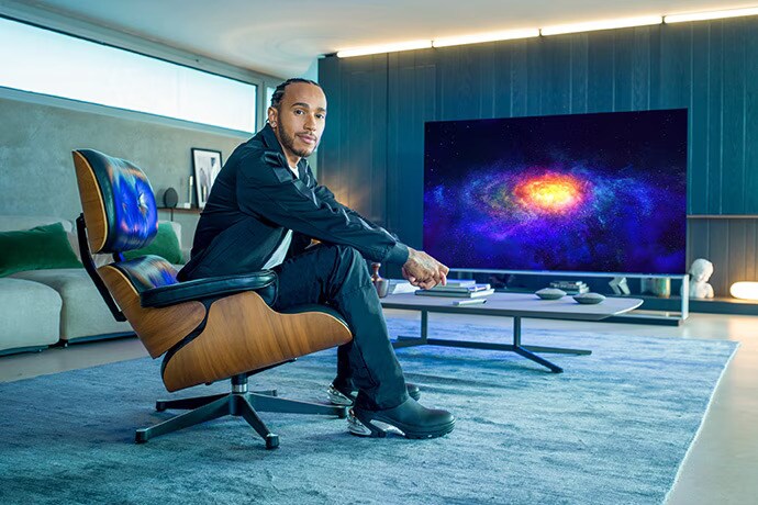 Lewis Hamilton sitter i en soffa med LG SIGNATURE OLED 8K tv:n bakom sig.