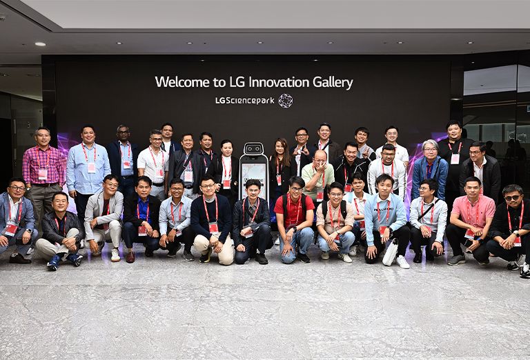 Group of people posing for a photo in front of the 'Welcome to LG Innovation Gallery' sign at LG Science Park.