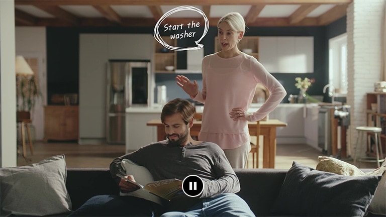 A woman is standing and talking to a man sitting on a sofa reading a book in the living room