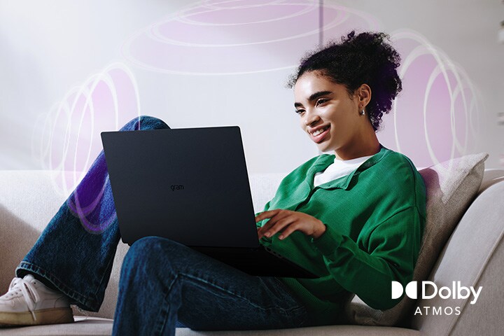 A person sitting on a couch, enjoying immersive audio while using an LG gram laptop. The text highlights Dolby Atmos technology, emphasizing a rich, expansive, 360-degree auditory experience. Surrounding sound waves in the background visually represent the immersive soundscape.
