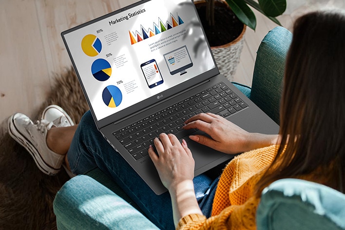 A person sitting comfortably in a chair, using a laptop that displays a presentation with charts and graphs. An animation demonstrates the anti-glare screen by showing no light reflection even when sunlight shines directly onto the display.