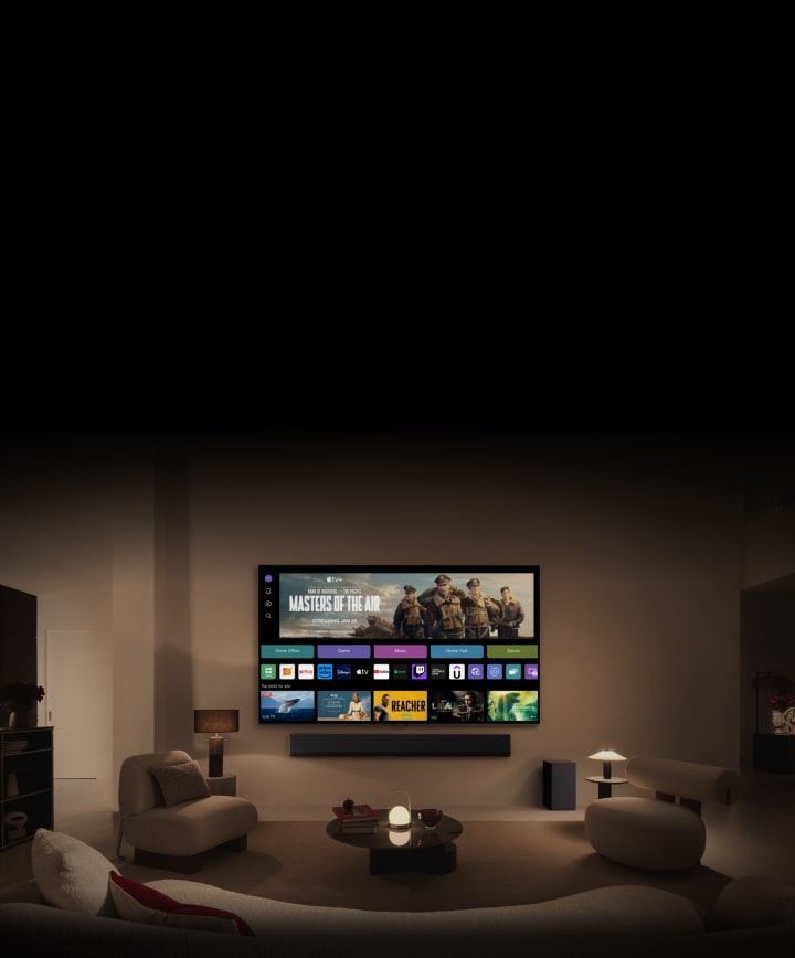 LG OLED TV showing the buttons Home Office, Game, and Music over a banner for Masters of the Air zooms out to show the TV mounted on a wall in a living room. The following logos are displayed on the TV screen in the image: LG Channels, Netflix, Prime Video, Disney TV, Apple TV, YouTube, Spotify, Twitch, GeForce Now and Udemy.