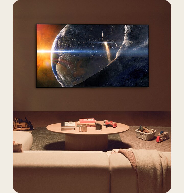 An image of a family sat on the floor of a low-lit living room by a small table, looking up at an LG TV mounted on the wall showing the Earth from space.