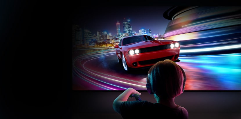 A young boy wearing headphones is seen from behind playing a car racing game on a large LG TV.
