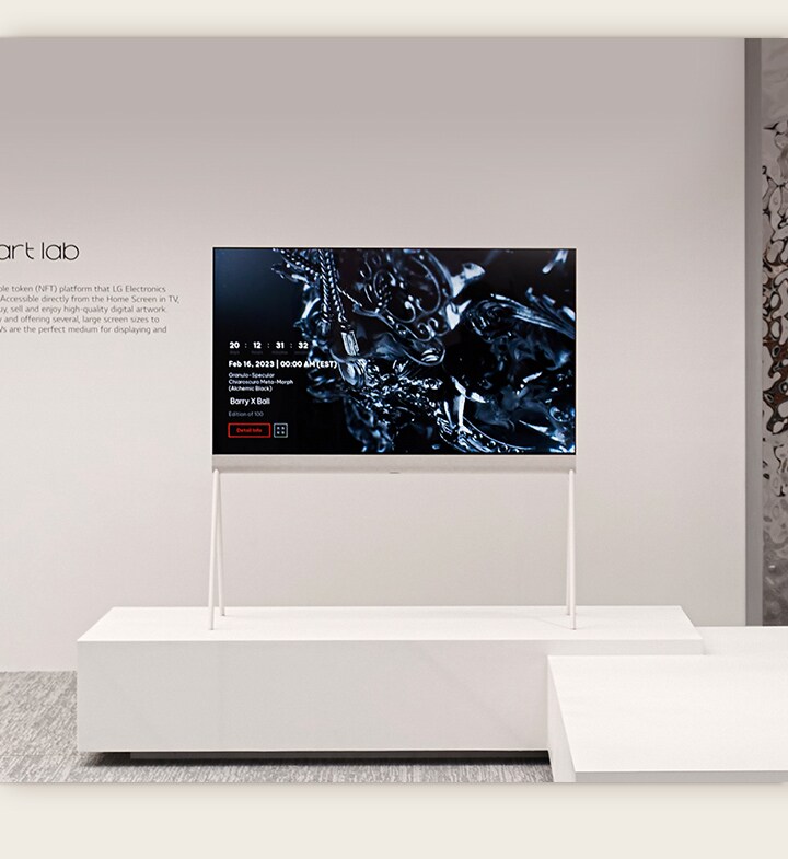 LG OLED Easel อยู่ในห้องสีขาวที่มีงานศิลปะดิจิทัลของรูปปั้นสีดำบนหน้าจอ ประติมากรรมสีเงินทางด้านขวามือของทีวีแสดงให้เห็นภาพสะท้อนของห้อง