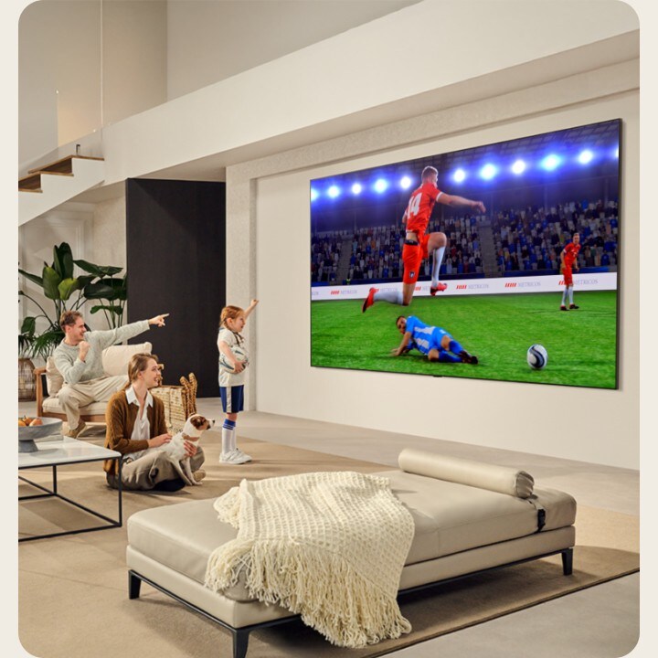 Oturma odasında bir aile. Neredeyse tüm duvarı kaplayan ultra büyük ekrana sahip duvara monta bir LG TV’ye sahipler. Büyük ve sürükleyici ekranda heyecan verici bir futbol maçı izliyorlar.  