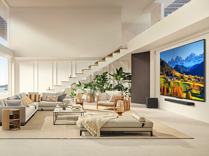 Modern bir yaşam alanında LG Soundbar üzerinde duvara monte LG QNED TV.  Zero Connect Box kahve sehpasının içinde duruyor.