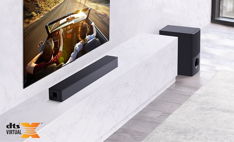 Duvarda TV; TV'nin altında beyaz mermer rafın üstünde LG Soundbar ve sağında subwoofer. Arabada giden bir çifti gösteren TV.