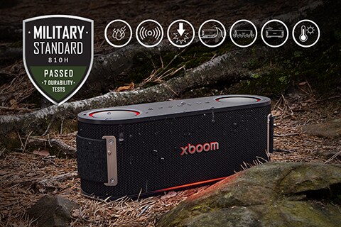 Islak yaprakların yanında, bir ağaç kökü ve bir taşın arasına yerleştirilmiş toprağın üzerinde bir xboom Bounce. Sol üst tarafta Askeri standart logosu bulunuyor.