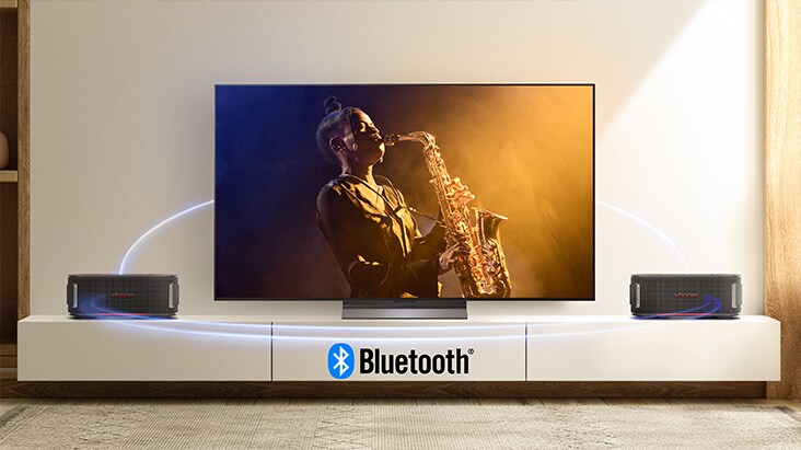 OLED C5 TV is on the wall showing concert scene and two units of xboom Bounce are placed on both side of the floor. Virtual blue light streak is connecting all 3 of them to show they're connected via bluetooth. 