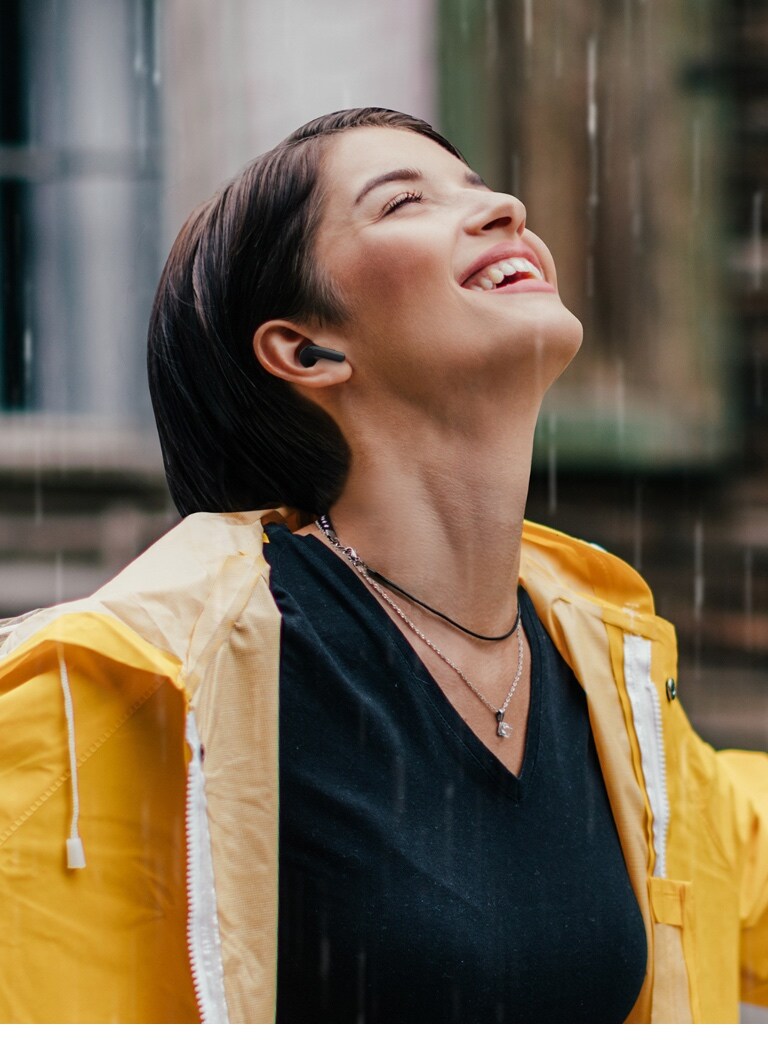 一名穿著亮色雨衣的女子站在雨中聽耳機。