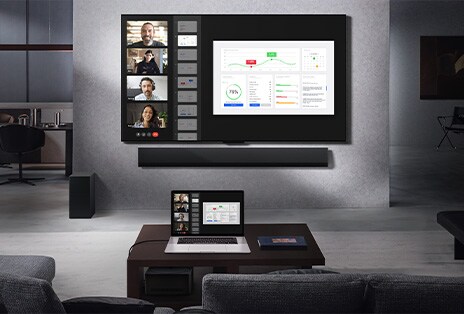 客廳的沙發上可以看到風景，對面是壁掛式 LG True Wireless 電視和 LG Soundbar。咖啡桌上有一台筆記型電腦，它連接到桌子下方幾乎看不見的零連接盒。具有即時視訊通話功能的筆記型電腦螢幕可以無線鏡像到電視螢幕上。整個空間整潔，沒有電線雜亂。