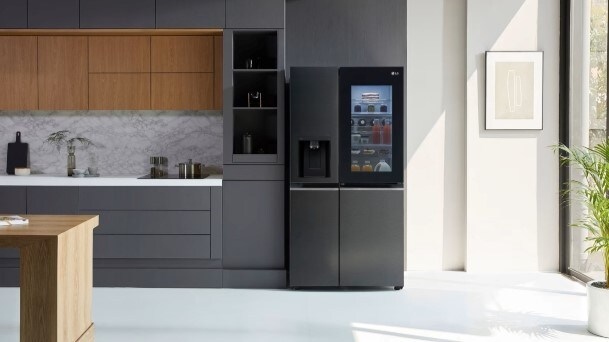 LG InstaView American-style fridge freezer with illuminated door panel in a modern kitchen with dark cabinets, marble backsplash, and natural light from a large window.