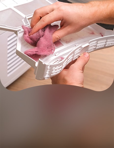 Close-up of hands removing pink lint from a dryer filter screen