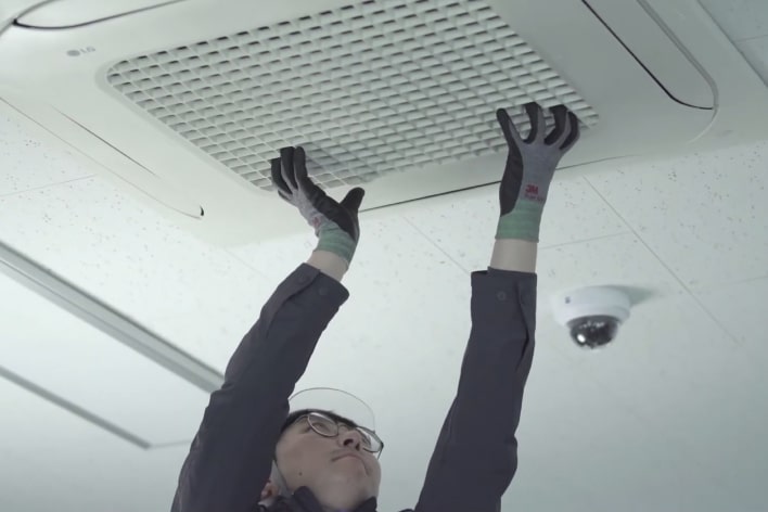 An installer wearing a safety helmet and glasses tries to separate the front panel of the Ceiling Mounted Cassette installed on the ceiling.