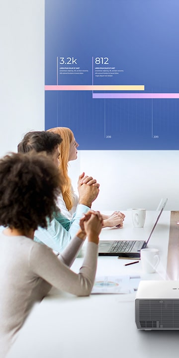 Five people are having a meeting in a bright room, viewing a vibrant display with the LG ProBeam projector.	