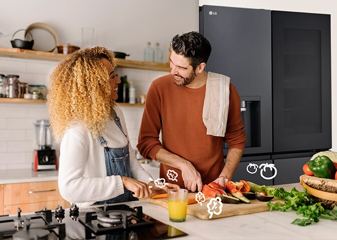 Una pareja sonriente cocina delante de la nevera.