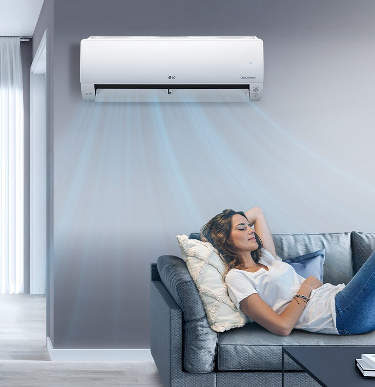 Woman reclining on a grey sofa, enjoying cool air from a wall-mounted LG air conditioner in a modern living room.