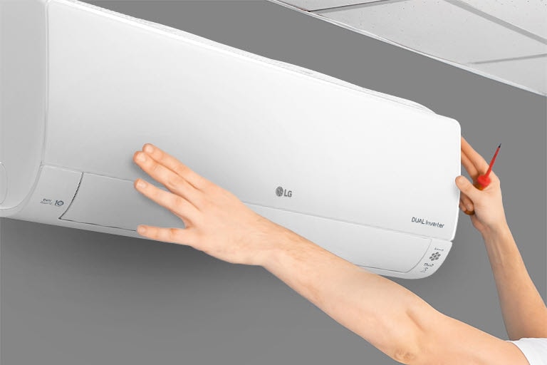 Technician adjusting a white LG Dual Inverter air conditioner on a grey wall with a screwdriver.