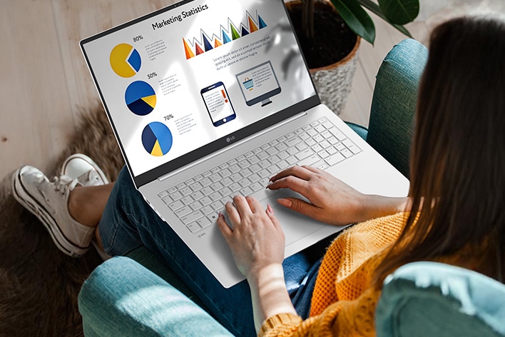 A person sitting comfortably in a chair, using a laptop that displays a presentation with charts and graphs. An animation demonstrates the anti-glare screen by showing no light reflection even when sunlight shines directly onto the display.