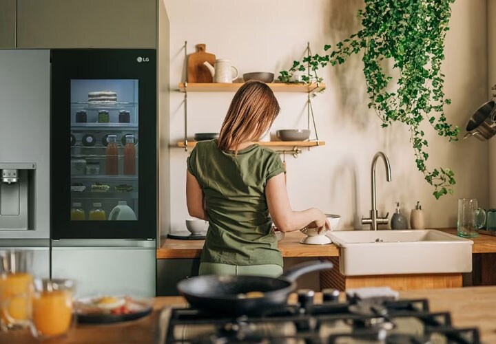 A woman in the kitchen using a see-through fridge