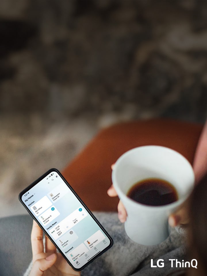 A person holding a smartphone displaying the LG ThinQ app while enjoying a cup of coffee.	