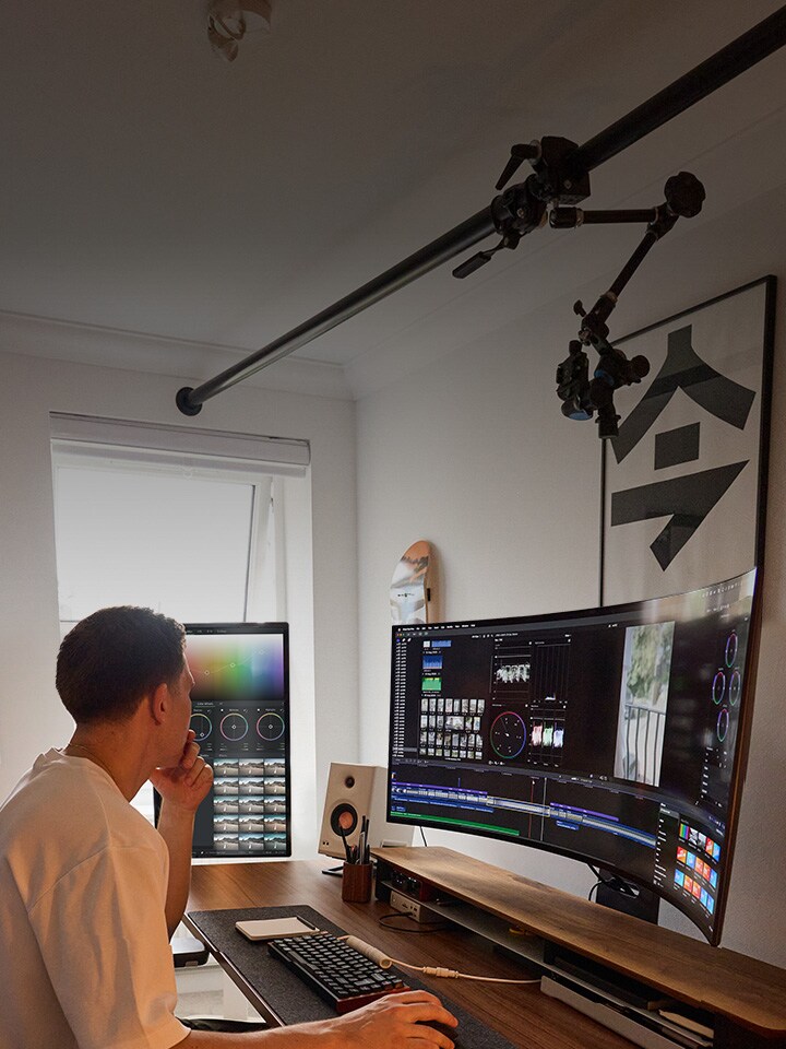 Man sitting at desk in room, editing video on computer monitor
