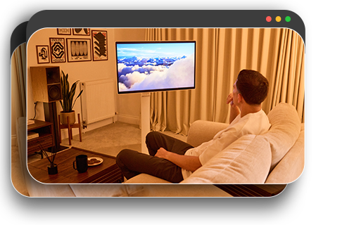 A man relaxing in a dimly lit room, watching a film on a monitor.