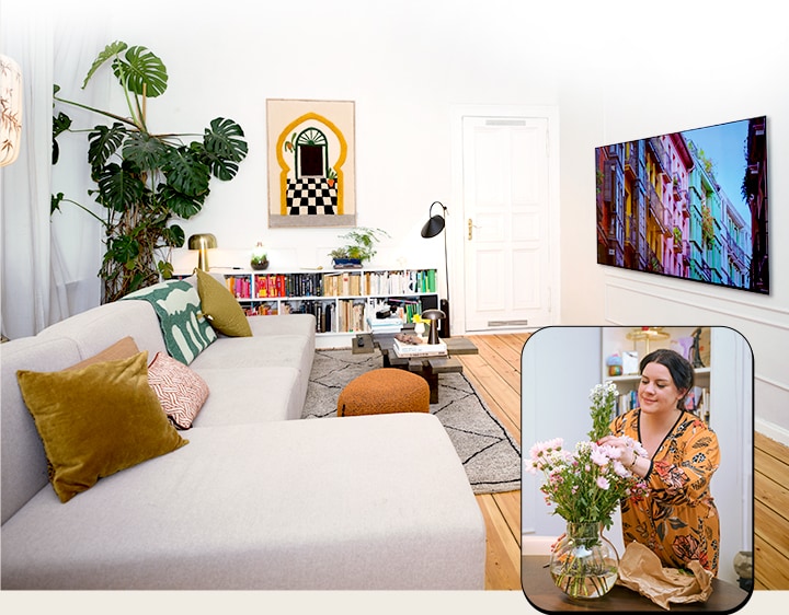This is an image showing a panoramic view of the living room with a TV next to a picture of a woman arranging flowers.