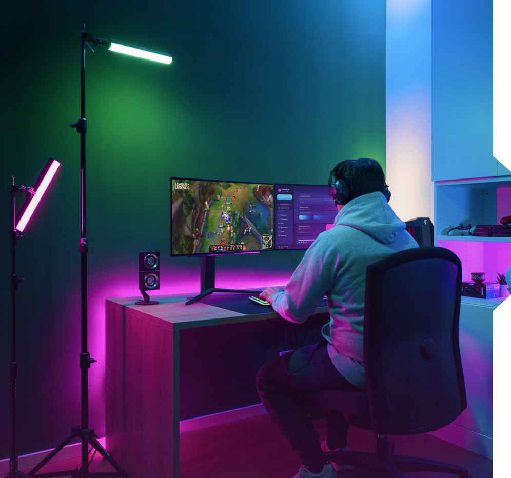 A gamer in a dark room with LED lights and a dual monitor setup.