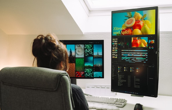 A woman working with two large monitors in a home office setup.