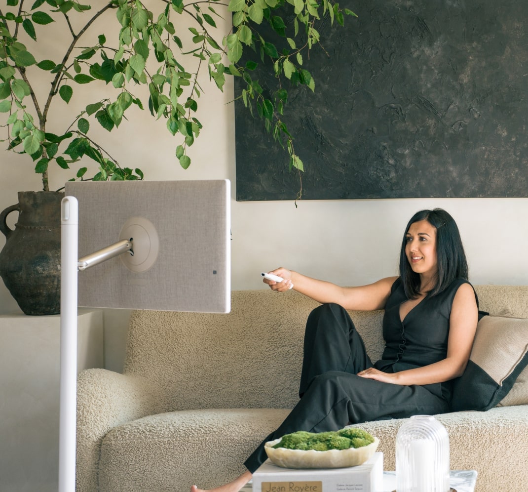 Lisa Mistry is reclining on her living room sofa, smiling as she uses a remote to control the LG StandbyME.