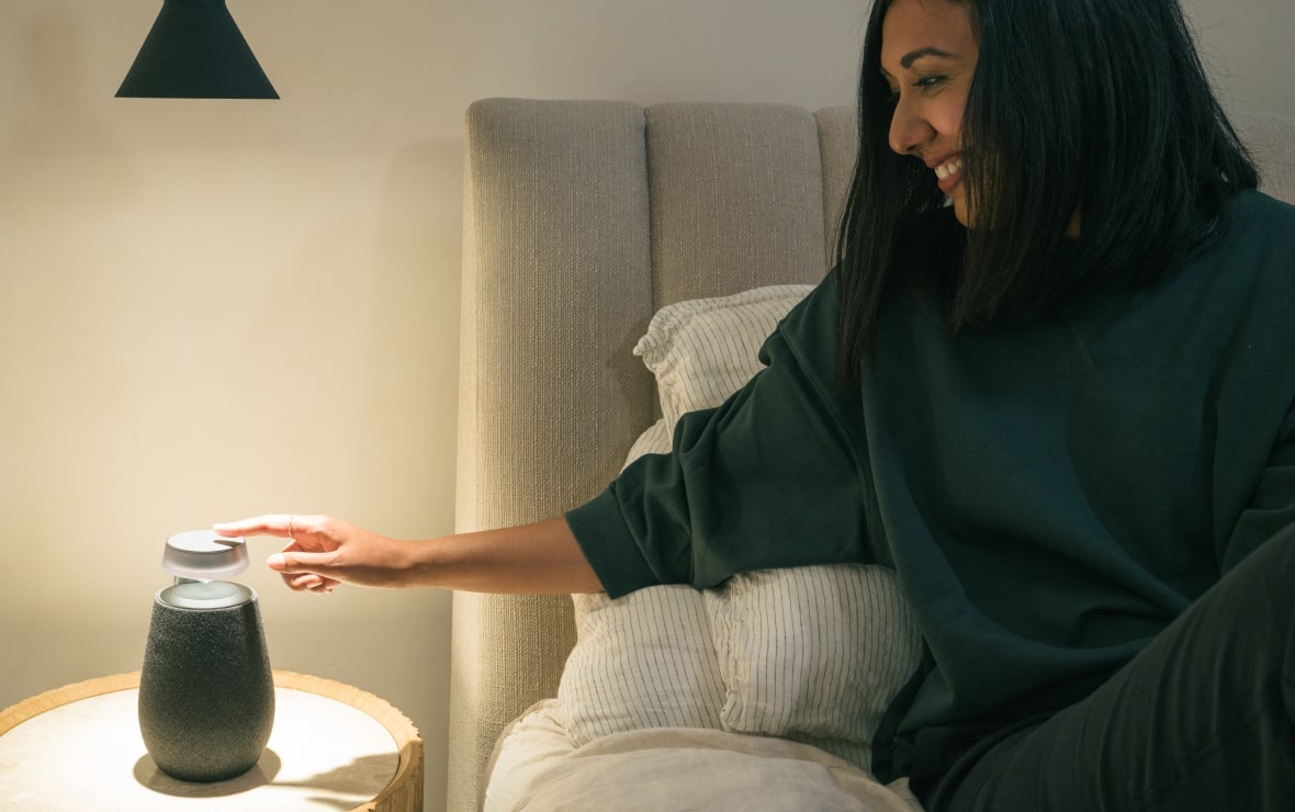 Lisa Mistry is reclining on her bed, touching the control pad of the LG Xboom XO2T with its Mood Lighting feature turned on.