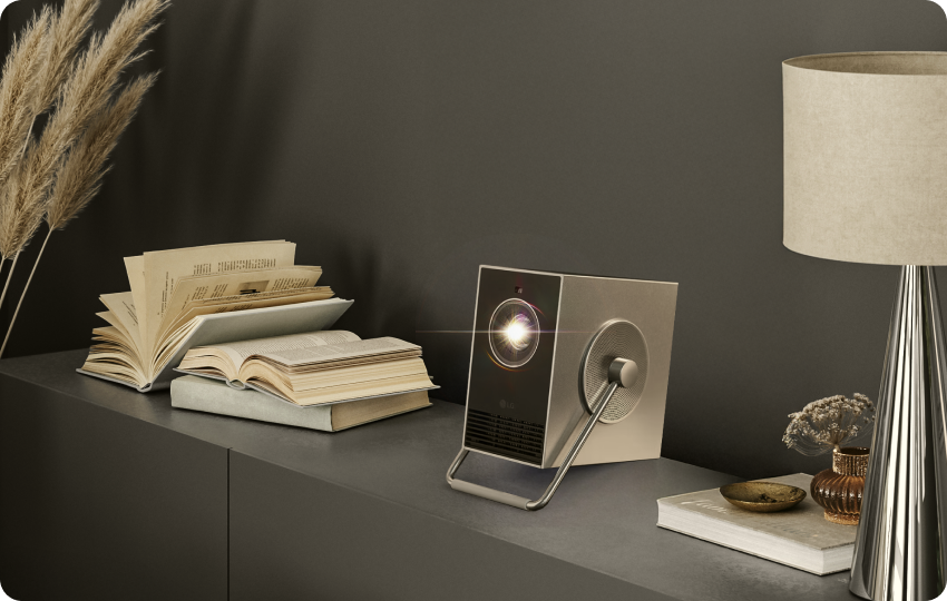 LG CineBeam Q projector placed on a shelf with books and decor in a stylish living space.