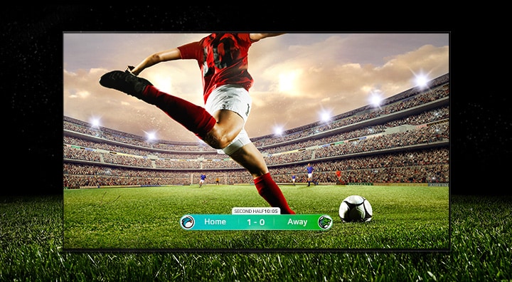 An image of the display showing a soccer game with a player in a red strip about to kick the ball across the stadium. The game score is visible at the bottom of the screen. The green grass from the pitch stretches beyond the screen to the black backdrop.