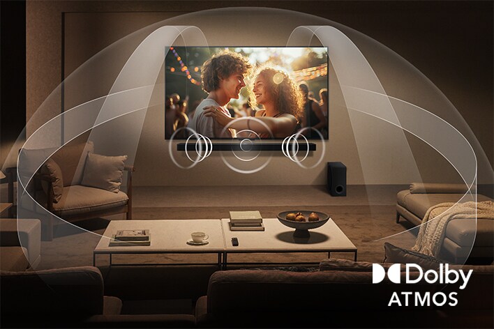 Phòng khách ấm cúng với ánh sáng dịu nhẹ nơi cặp đôi tận hưởng phim trên TV LG QNED và Soundbar LG. Đồ họa mô phỏng Dolby Atmos lan tỏa âm thanh vòm từ mọi hướng. Biểu tượng Dolby Atmos ở góc dưới.