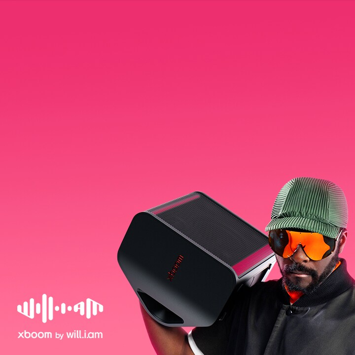 will.i.am mặc trang phục đen và đeo kính râm, đang vác chiếc XBOOM Stage 301 trên vai.