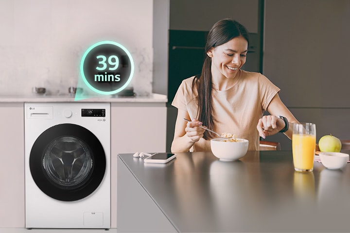 Người phụ nữ đang ngồi ở bàn nhìn vào đồng hồ và có một chiếc máy giặt phía sau	